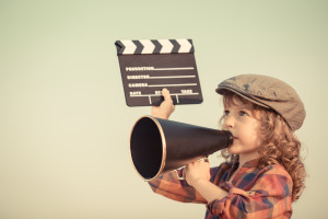 Kid holding clapper board and shouting through vintage megaphone. Cinema concept. Retro style